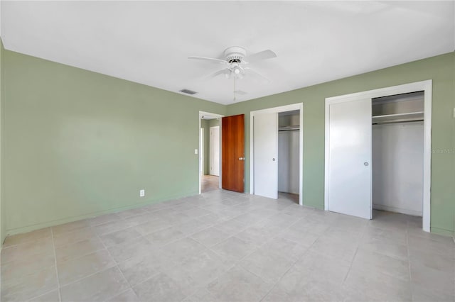 unfurnished bedroom featuring ceiling fan, light tile patterned floors, and two closets