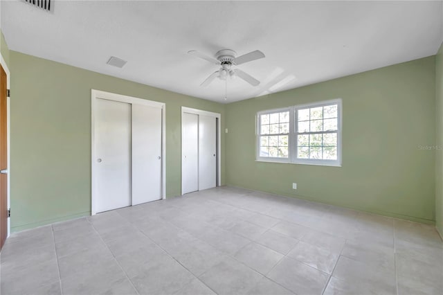 unfurnished bedroom featuring ceiling fan, light tile patterned floors, and two closets