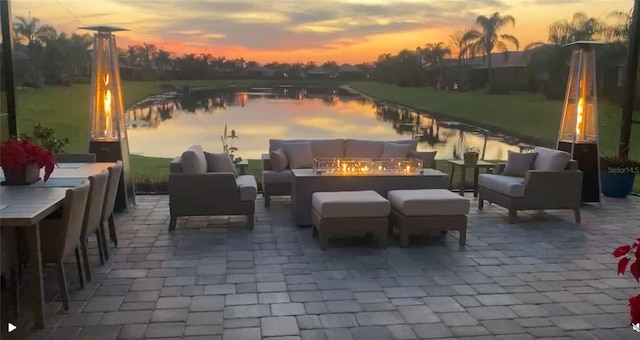 patio terrace at dusk featuring a water view and an outdoor living space with a fire pit