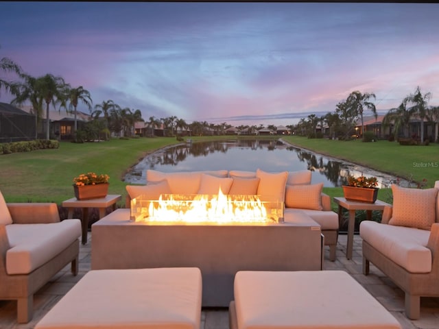 patio terrace at dusk featuring a yard, a water view, and an outdoor living space with a fire pit