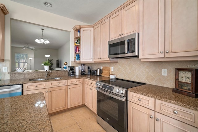 kitchen featuring sink, stainless steel appliances, dark stone counters, light brown cabinetry, and ceiling fan with notable chandelier