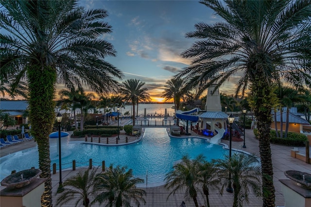 pool at dusk featuring a patio area, a water view, and a water slide