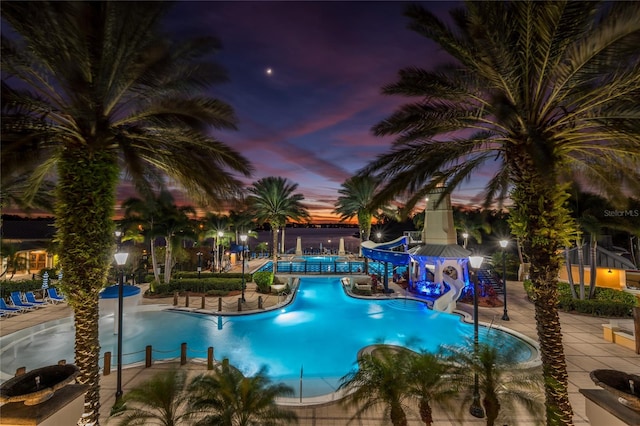 pool at dusk featuring a patio area and a water slide