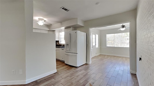 kitchen with light wood-type flooring, white appliances, white cabinetry, and brick wall