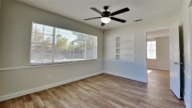 unfurnished room with built in shelves, light wood-type flooring, ceiling fan, and a healthy amount of sunlight