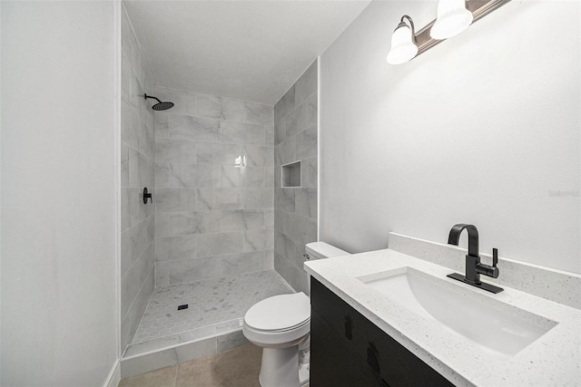 bathroom with tiled shower, vanity, toilet, and tile patterned flooring