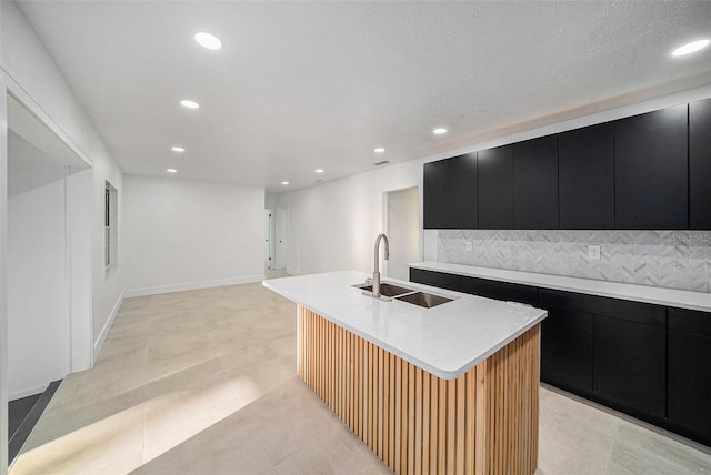 kitchen with a textured ceiling, a center island with sink, tasteful backsplash, and sink