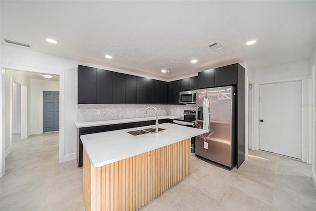 kitchen with decorative backsplash, a textured ceiling, stainless steel appliances, a kitchen island with sink, and sink