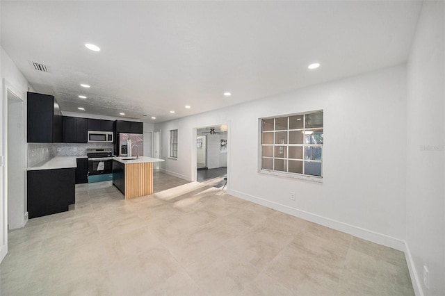 kitchen with ceiling fan, decorative backsplash, an island with sink, a kitchen bar, and stainless steel appliances