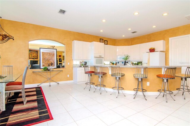 kitchen featuring white cabinets, a kitchen breakfast bar, light tile patterned flooring, and white appliances