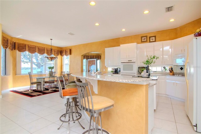 kitchen featuring pendant lighting, white appliances, white cabinets, light tile patterned floors, and an island with sink