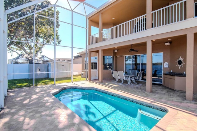 view of swimming pool featuring ceiling fan, a storage shed, a patio, and glass enclosure