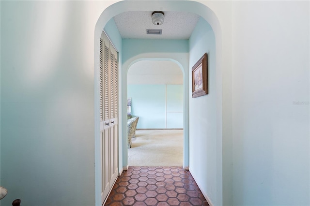 hall with a textured ceiling and dark carpet