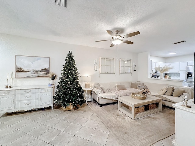 living room with a textured ceiling, ceiling fan, and light tile patterned flooring