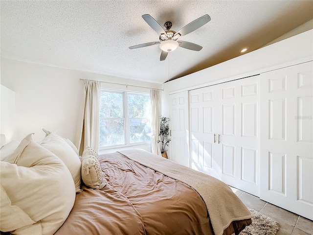 tiled bedroom with ceiling fan, lofted ceiling, a textured ceiling, and a closet