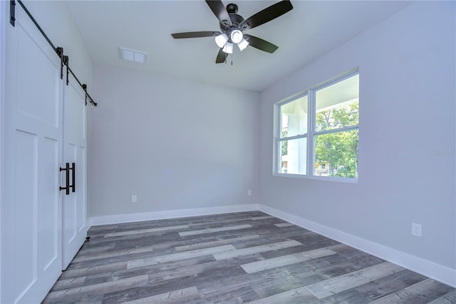 empty room featuring a barn door, ceiling fan, and dark hardwood / wood-style flooring