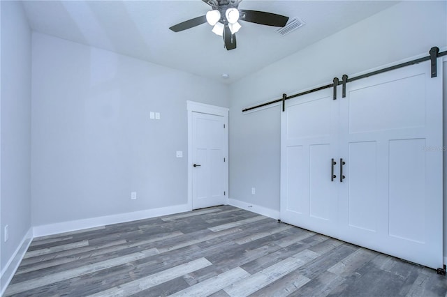 unfurnished bedroom featuring a barn door, a closet, ceiling fan, and hardwood / wood-style flooring