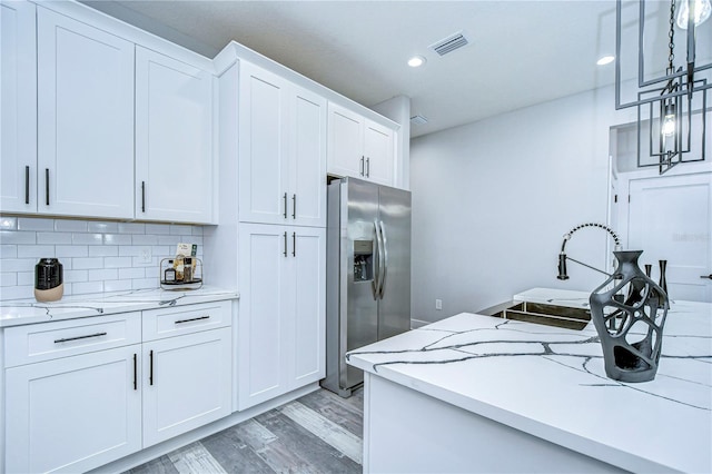 kitchen featuring white cabinetry, light stone countertops, tasteful backsplash, stainless steel fridge with ice dispenser, and light wood-type flooring