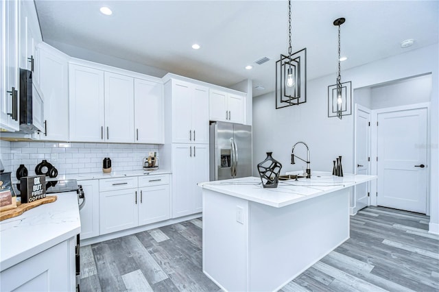 kitchen with stainless steel fridge, a center island with sink, and white cabinets