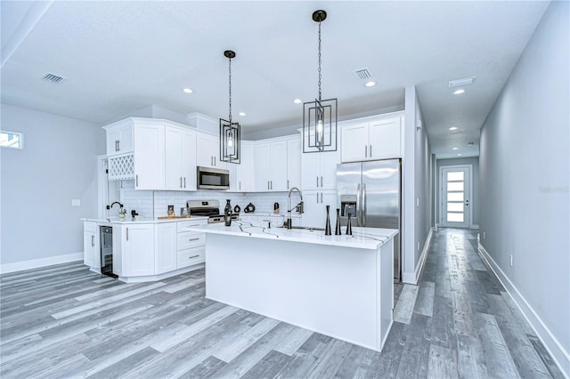 kitchen featuring backsplash, hanging light fixtures, an island with sink, appliances with stainless steel finishes, and white cabinetry