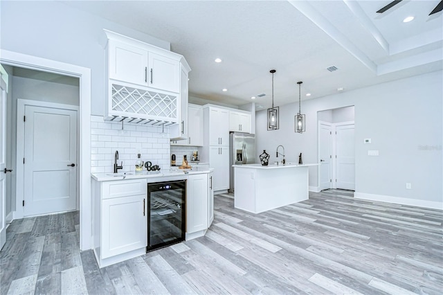 kitchen featuring hanging light fixtures, white cabinets, a kitchen island, and beverage cooler