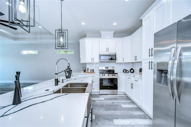 kitchen with white cabinets, sink, hanging light fixtures, light stone counters, and stainless steel appliances