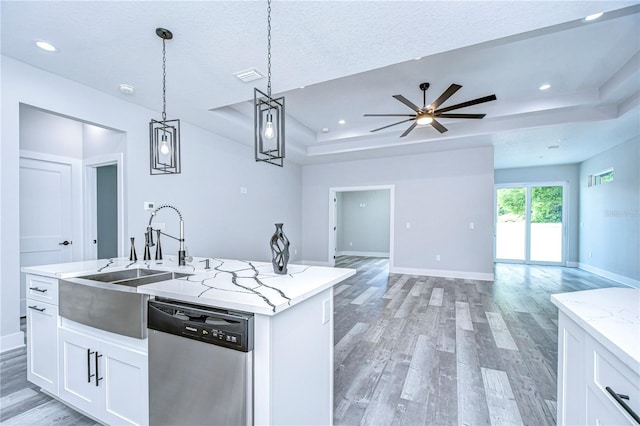 kitchen with stainless steel dishwasher, a tray ceiling, a kitchen island with sink, decorative light fixtures, and white cabinets