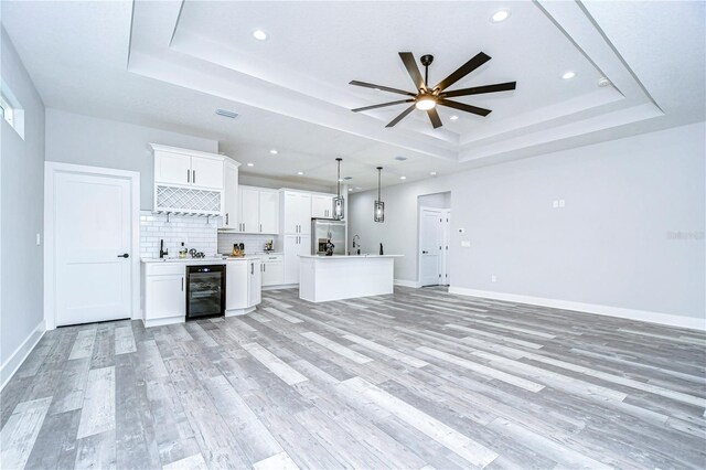 interior space featuring wine cooler, ceiling fan, light wood-type flooring, a tray ceiling, and indoor wet bar