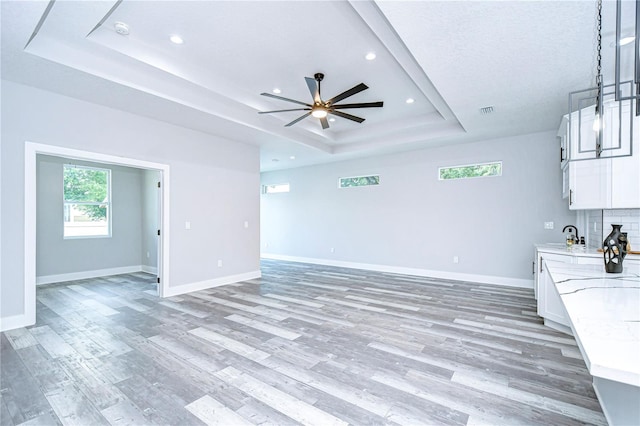 unfurnished living room with ceiling fan, wood-type flooring, and a tray ceiling