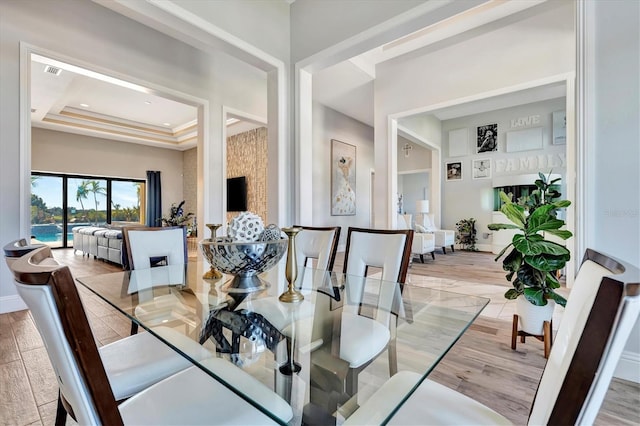 dining room with light hardwood / wood-style floors, a raised ceiling, and ornamental molding