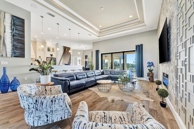 living room featuring ornamental molding, light hardwood / wood-style floors, a raised ceiling, and a stone fireplace