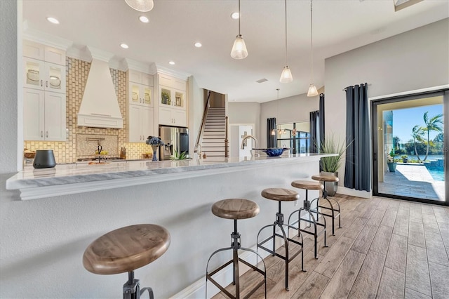 kitchen featuring premium range hood, white cabinetry, a breakfast bar, and decorative light fixtures