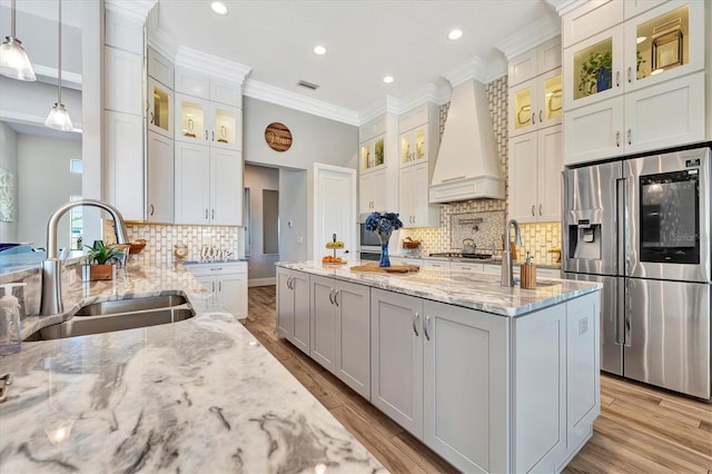 kitchen featuring light stone countertops, sink, hanging light fixtures, custom exhaust hood, and appliances with stainless steel finishes