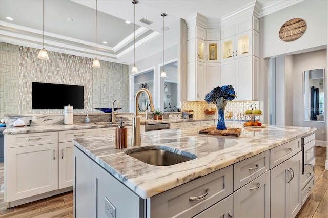 kitchen featuring light stone countertops, sink, light hardwood / wood-style flooring, white cabinetry, and an island with sink