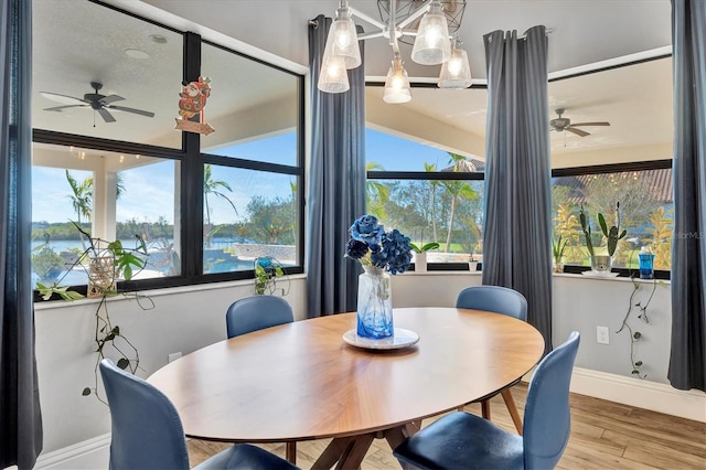 dining space with wood-type flooring, a water view, ceiling fan, and a healthy amount of sunlight