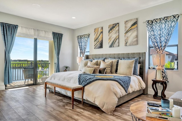 bedroom featuring hardwood / wood-style flooring, a water view, access to exterior, and multiple windows