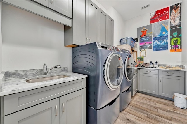 laundry area featuring cabinets, light hardwood / wood-style flooring, washer and dryer, and sink