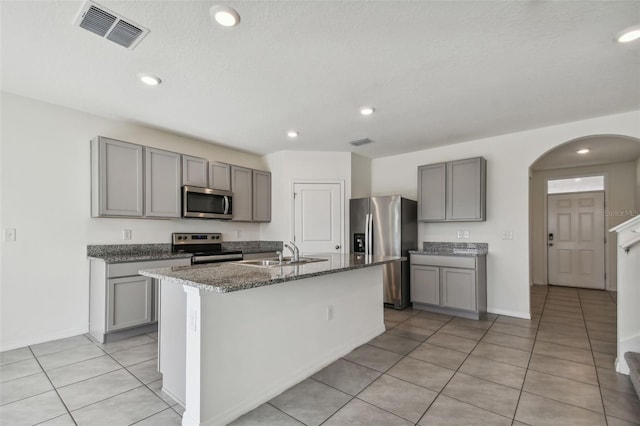 kitchen featuring gray cabinetry, sink, stainless steel appliances, a center island with sink, and light tile patterned floors