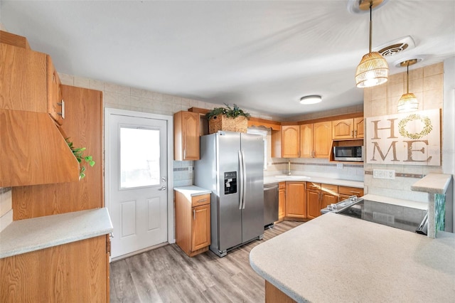 kitchen with decorative backsplash, light hardwood / wood-style floors, hanging light fixtures, and stainless steel appliances