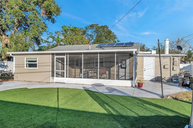 rear view of house with solar panels, a sunroom, a patio area, and a lawn