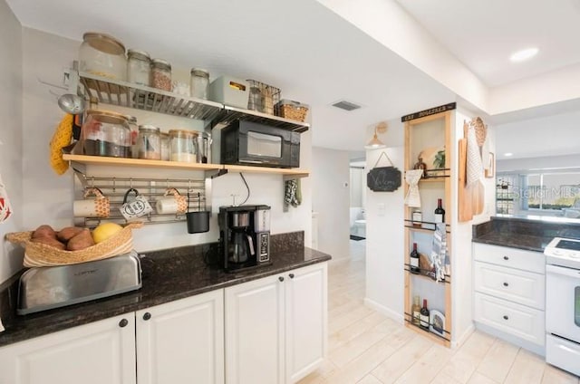 interior space featuring white electric range oven, light hardwood / wood-style floors, white cabinetry, and dark stone counters