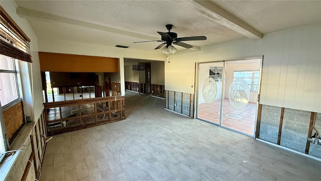 unfurnished room featuring wood walls, hardwood / wood-style flooring, ceiling fan, a textured ceiling, and beamed ceiling