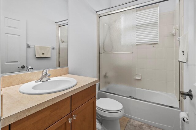 bathroom with toilet, tile patterned flooring, enclosed tub / shower combo, and vanity