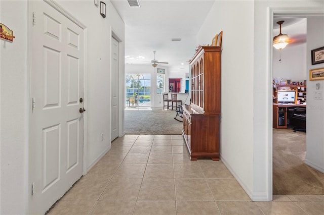 hall with light tile patterned floors, baseboards, visible vents, and light colored carpet