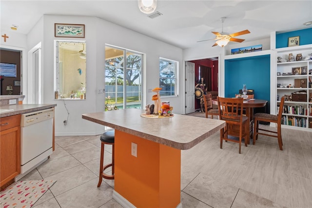 kitchen featuring light tile patterned floors, a breakfast bar area, visible vents, a center island, and dishwasher