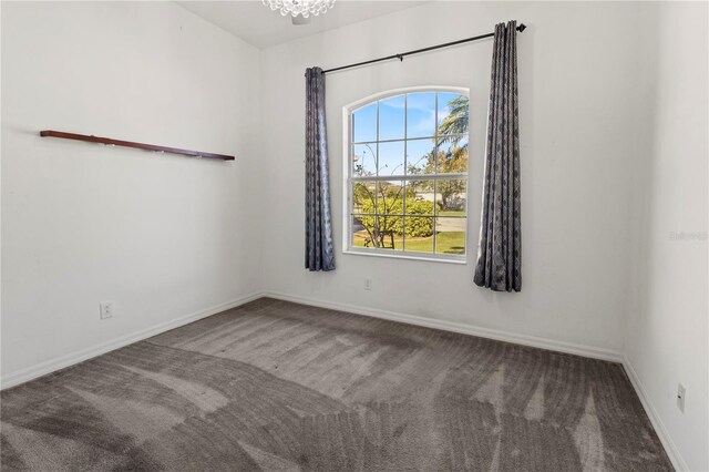 carpeted empty room featuring a chandelier and baseboards