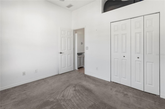 unfurnished bedroom with visible vents, baseboards, a high ceiling, carpet flooring, and a closet