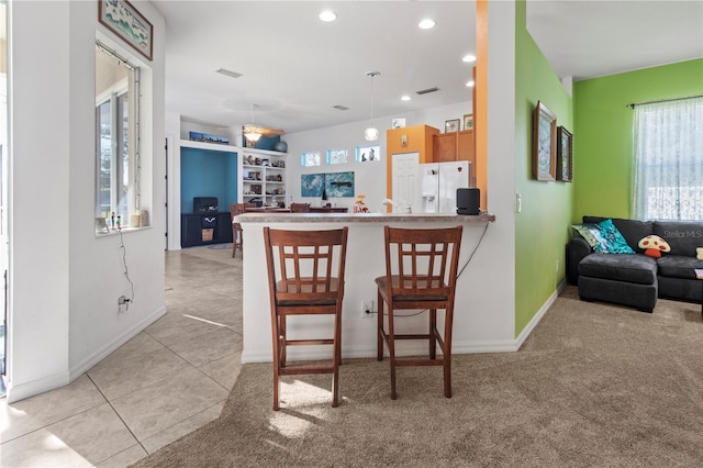 kitchen with a peninsula, white refrigerator with ice dispenser, open floor plan, a kitchen bar, and decorative light fixtures