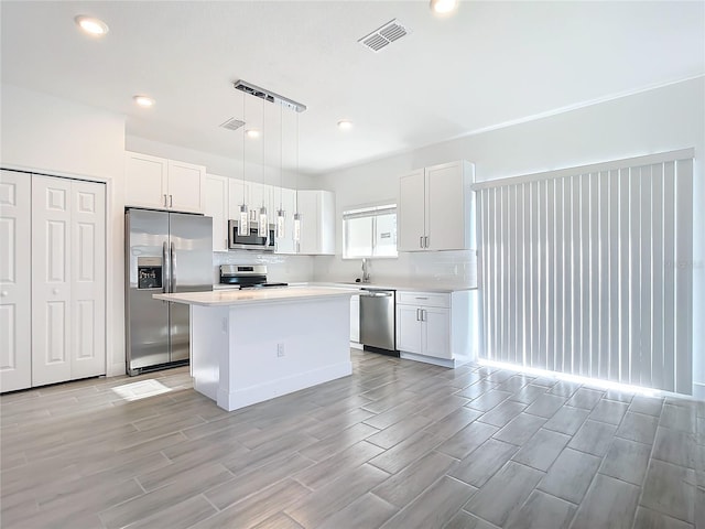 kitchen featuring appliances with stainless steel finishes, white cabinetry, a kitchen island, and pendant lighting