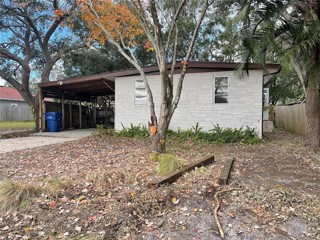 view of home's exterior with brick siding, an attached carport, driveway, and fence